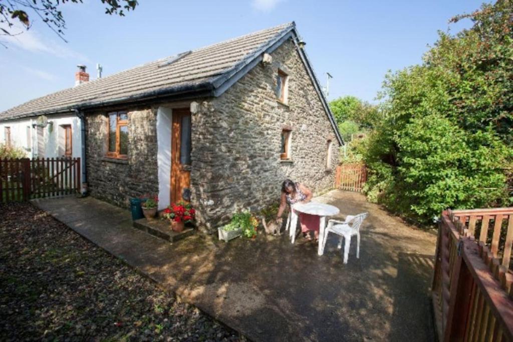 a woman sitting at a table in front of a house at Inviting 2-Bed Cottage in Newcastle Emlyn in Newcastle Emlyn