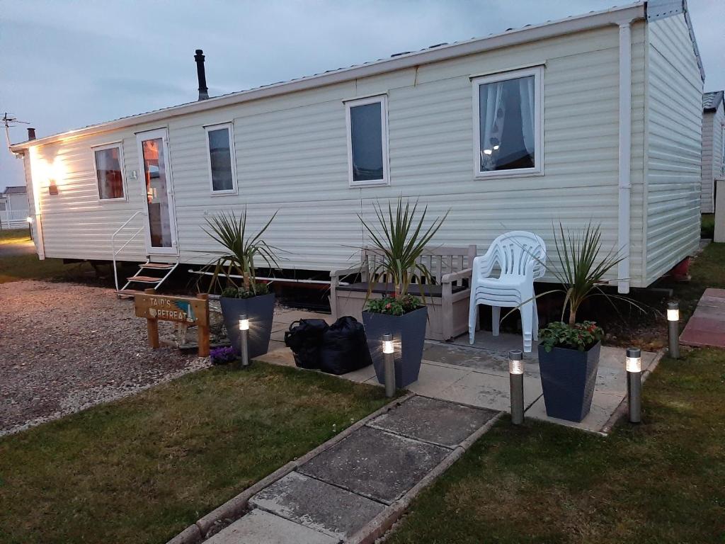 una casa blanca con una silla y algunas plantas en Taid's Retreat Silversands Cove beach lossiemouth en Lossiemouth