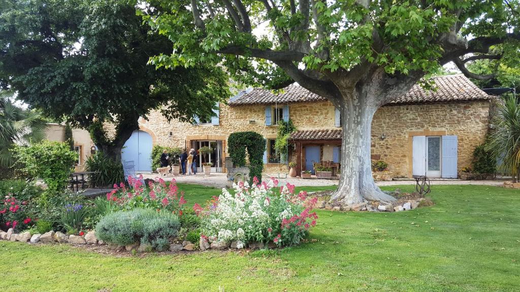 a stone house with a tree and flowers in the yard at Mas du Clos de l'Escarrat in Jonquières