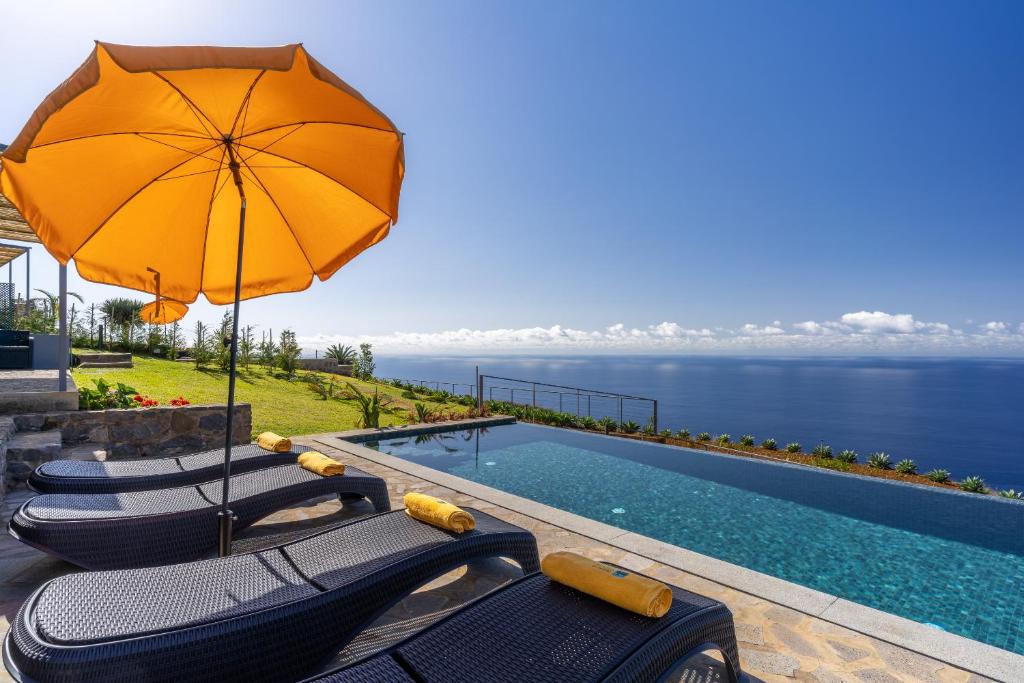 a pool with chairs and an umbrella and the ocean at Villa Flora Calheta Sunset & Ocean Views in Jardim do Mar