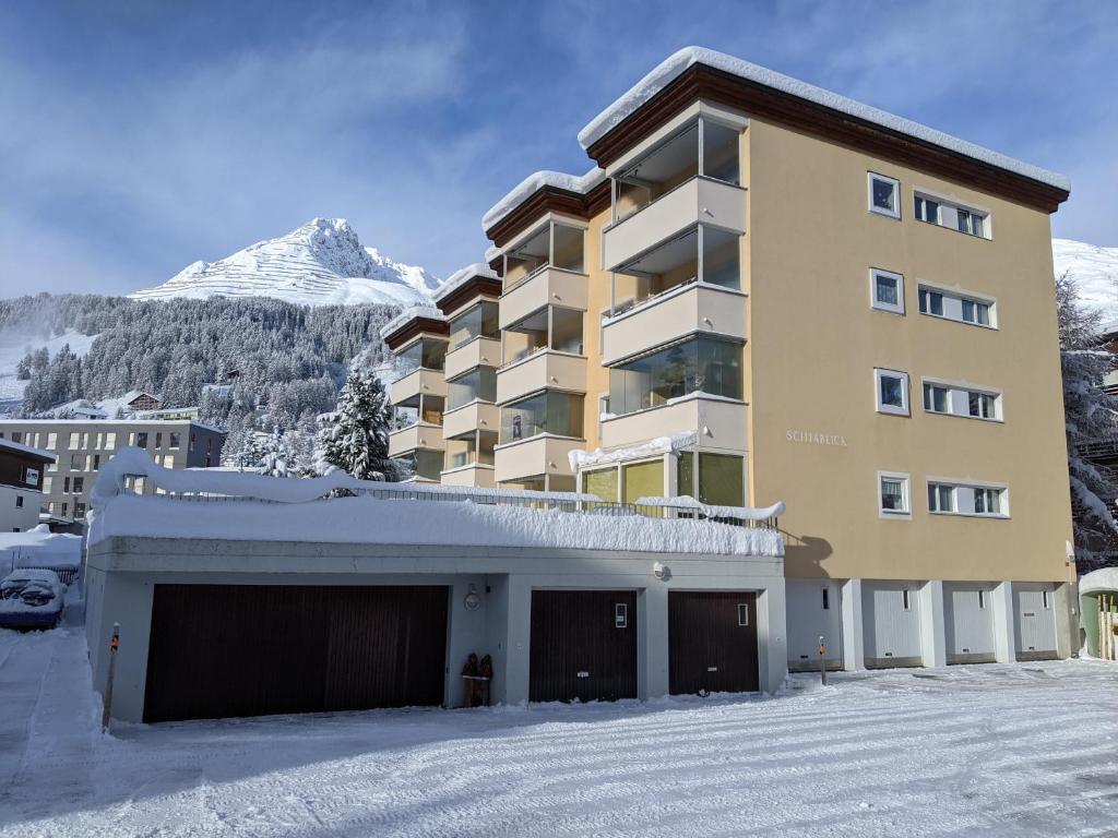 un grand bâtiment dans la neige devant une montagne dans l'établissement Schiablick - Broggini, à Davos