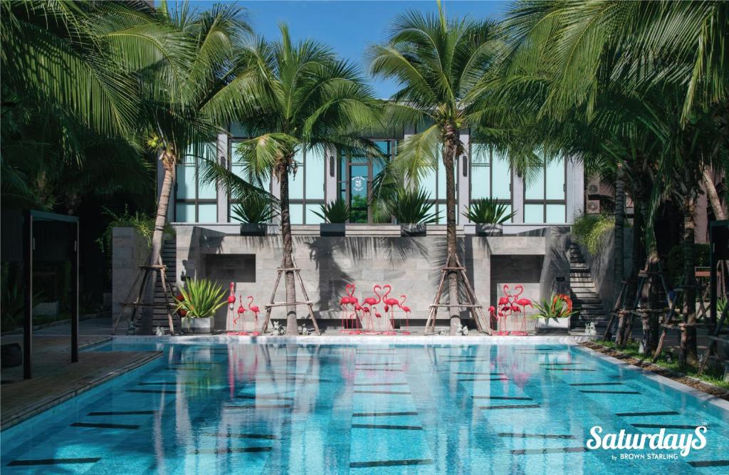 a swimming pool with palm trees in front of a building at Saturdays Residence by Brown Starling in Rawai Beach