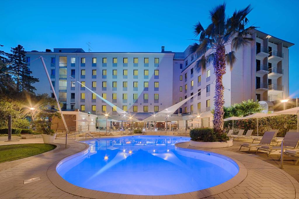 uma piscina em frente a um hotel com uma palmeira em NH Palermo em Palermo