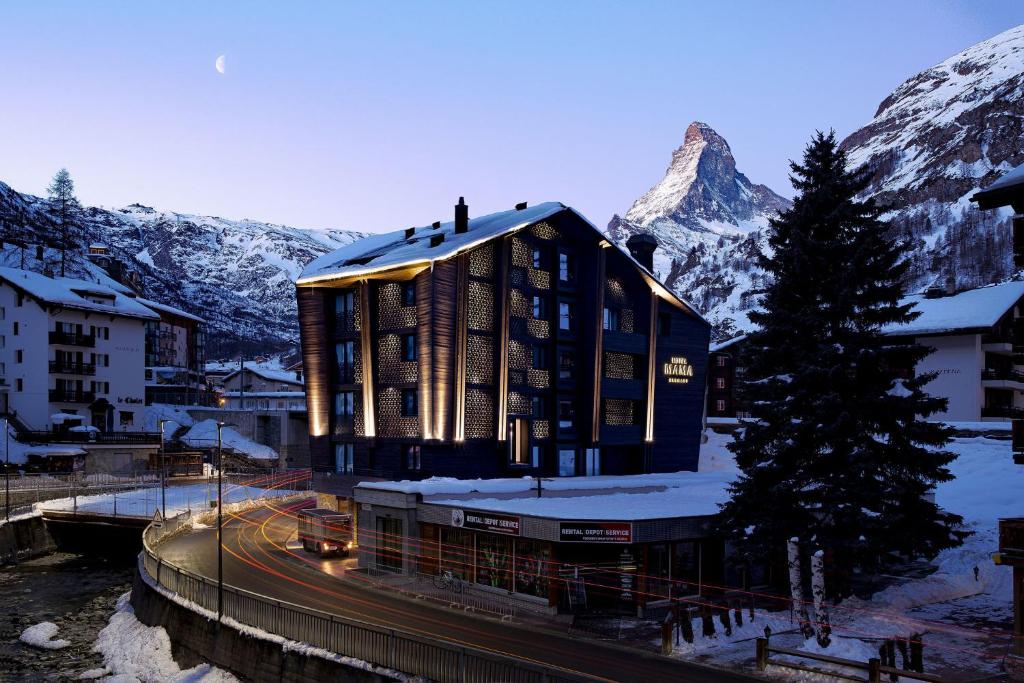 a building in front of a mountain with snow at Hotel ZERMAMA Zermatt in Zermatt