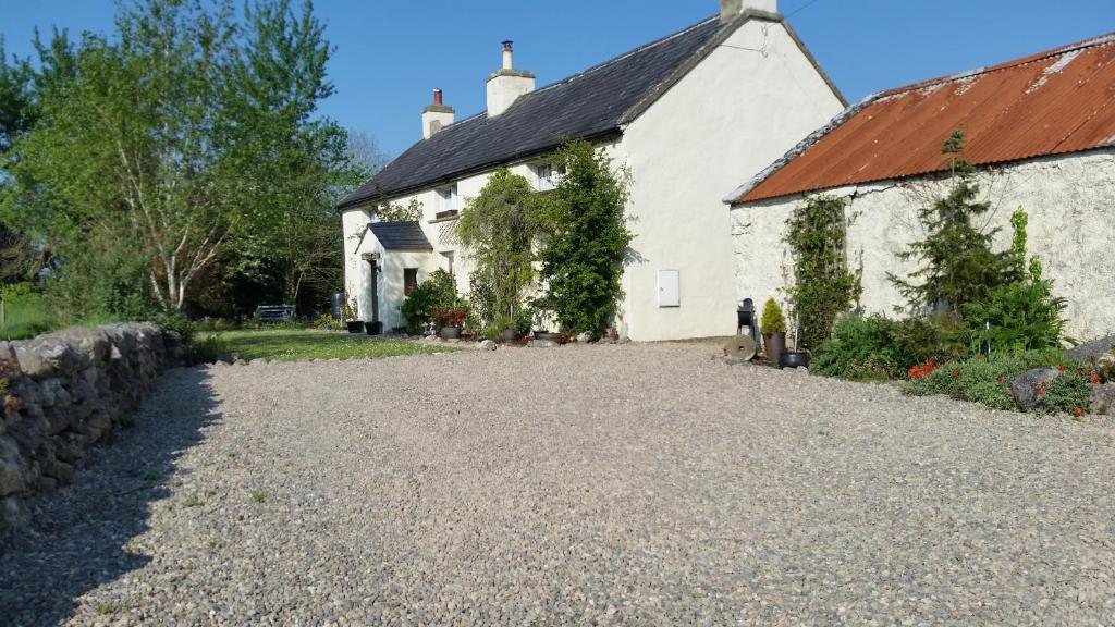 a white building with a gravel driveway next to it at Beautiful 300 year old traditional country cottage in Courtmatrix