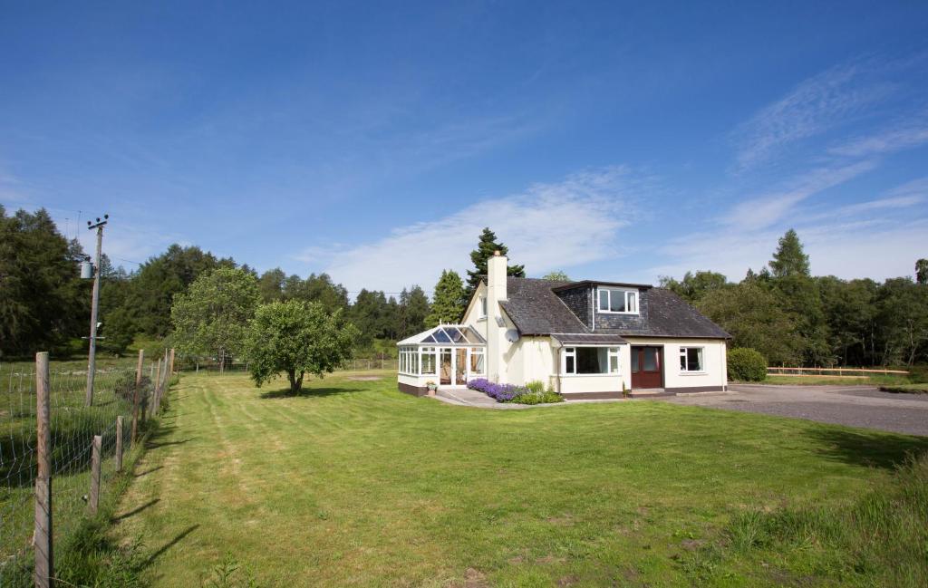 une petite maison blanche avec une cour herbeuse dans l'établissement Juniper Hill near Loch Achilty on the NC500, à Contin