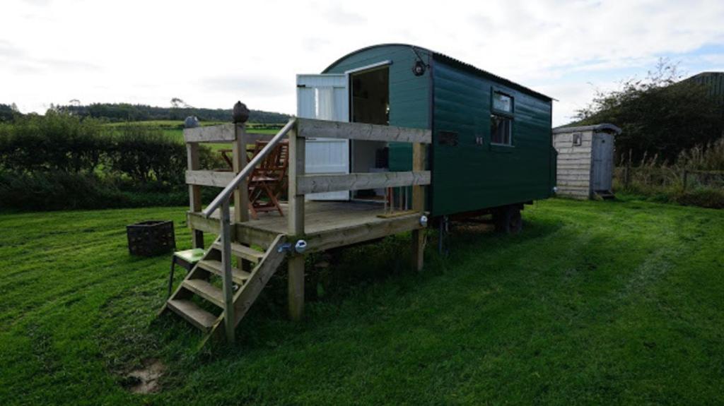a green tiny house with a staircase in a yard at Shepherd's Hut Westcote in Hawick