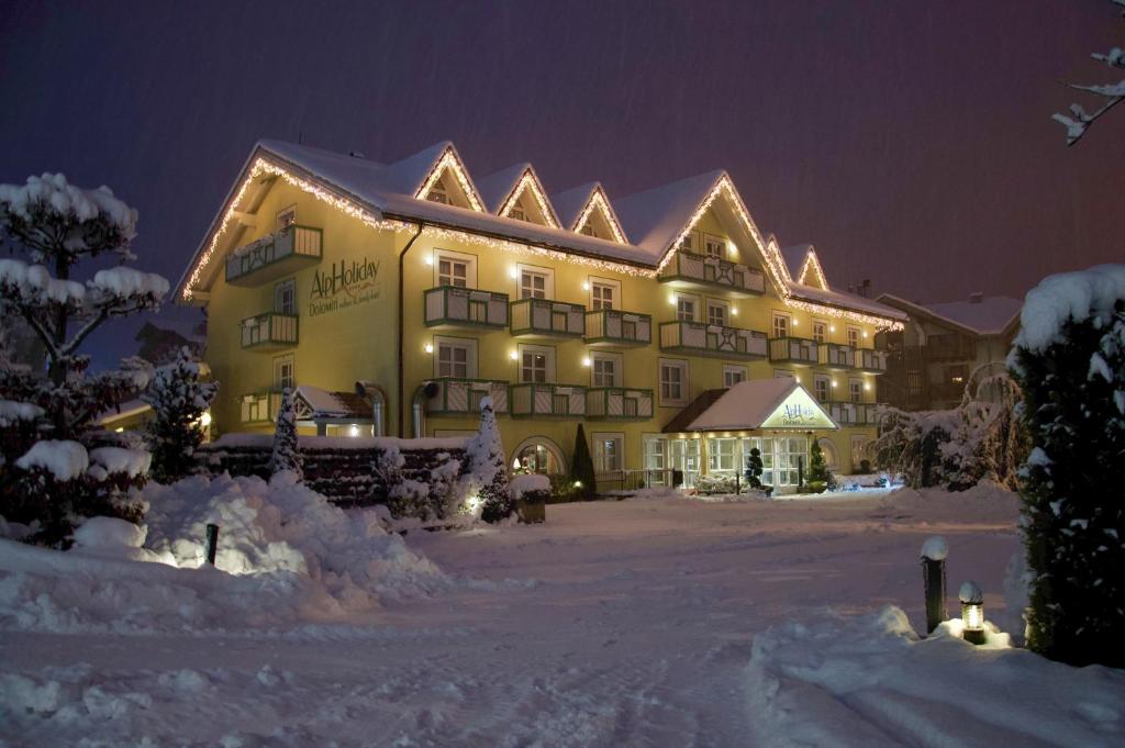 a large yellow building in the snow at night at Alpholiday Dolomiti Wellness & Family Hotel in Dimaro