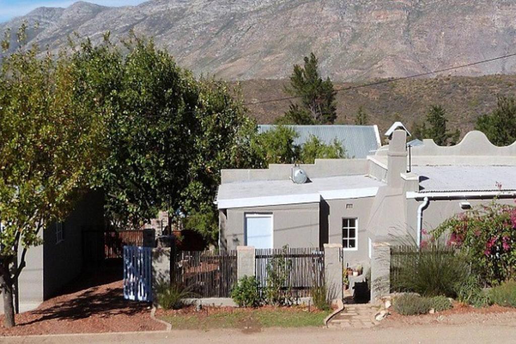 a white house with a fence in front of a mountain at Cosy 6 Person Cottage with Mountain View in Barrydale