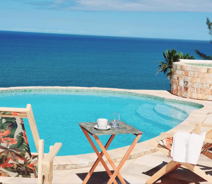 a pool with a table and chairs next to the ocean at Casa do Maracuja in Maricá