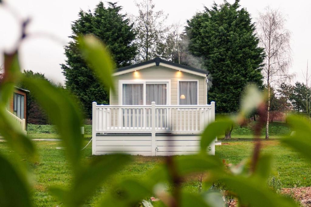 a small white cabin in a yard with trees at Yew Tree Lodge with Hot Tub in York