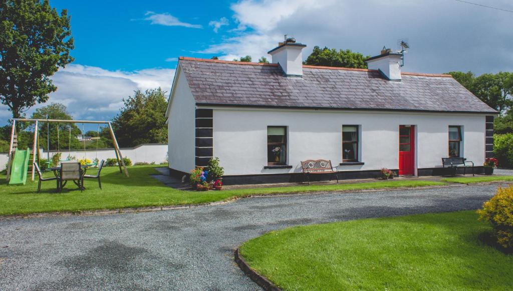 a small white house with a swing at Stunning 3-Bedroom House with Private Garden in Carracastle