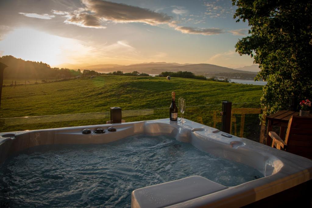 a jacuzzi tub with a bottle of wine at Super King Lodge-Sleeps 2-HotTub-Sea View in Langbank