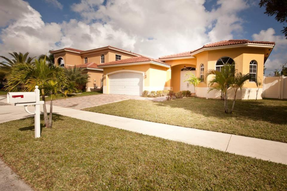 a large yellow house with a driveway at Aventura Home by Flatsaway in Aventura