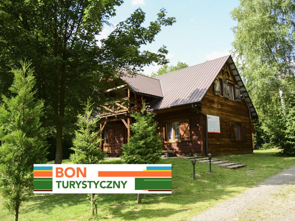 a wooden house with a sign in front of it at Witalna Osada Helonowo in Ropienka