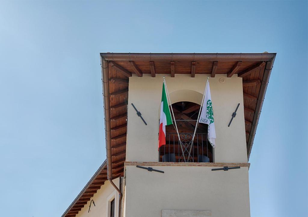 una torre dell'orologio con due bandiere di Residenza Cappelli - Case Vacanze a San Demetrio neʼ Vestini