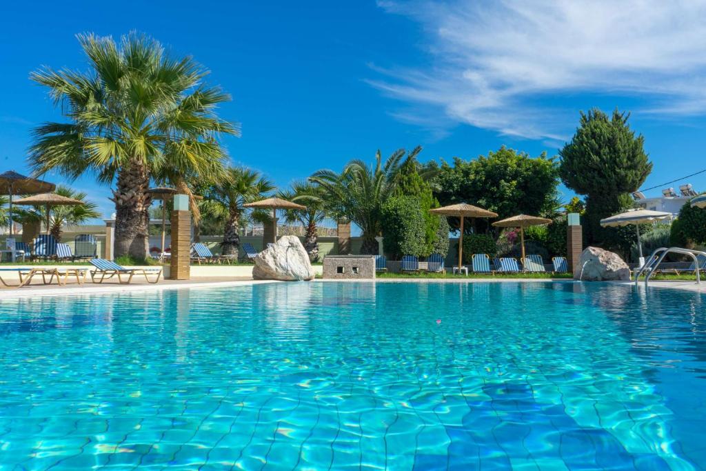 a large swimming pool with palm trees and umbrellas at Stamos All Inclusive in Faliraki