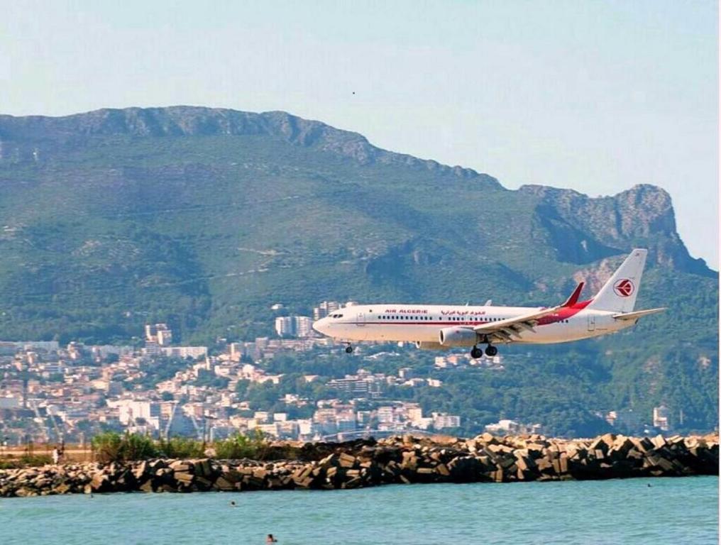 a plane flying over the water with a mountain in the background at Saldae Gîte Appartement in Bejaïa