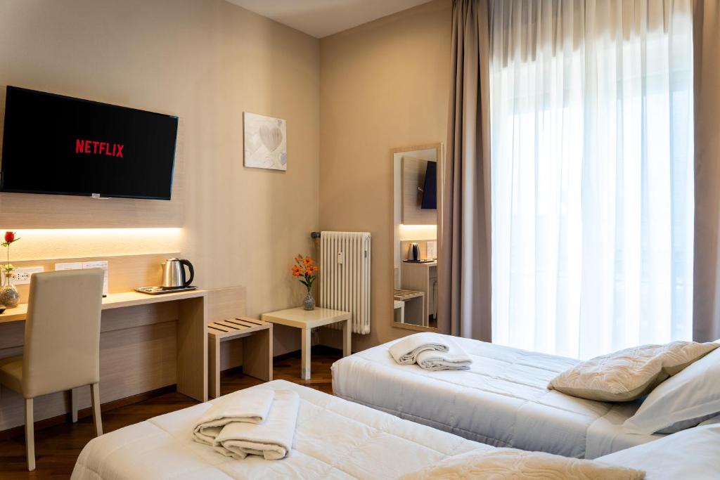 a hotel room with two beds and a desk at Hotel Victoria in Cuneo