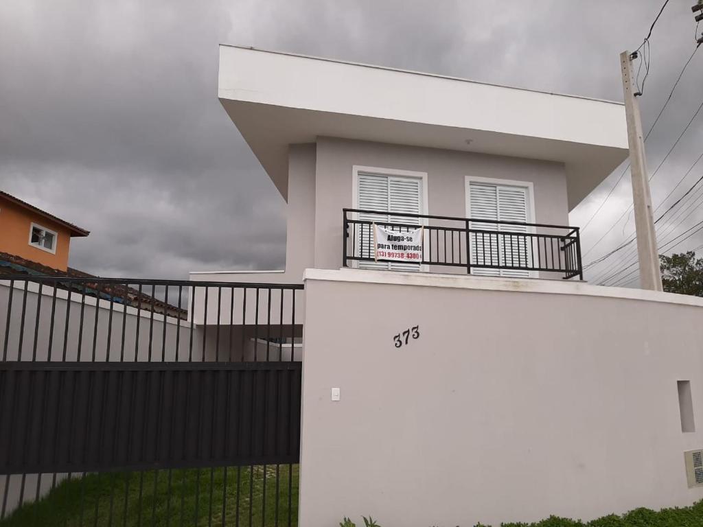 ein weißes Haus mit einem Balkon und einem Zaun in der Unterkunft Sobrado frente ao SESC, WIFI 300MB, 2 vagas auto, cozinha, churrasqueira, moderno e reformado in Bertioga