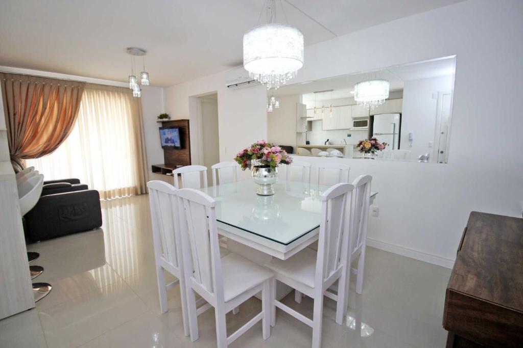 comedor con mesa de cristal y sillas blancas en Ipê Branco, en Bombinhas