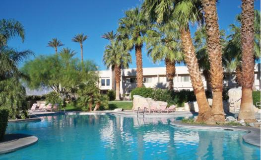 a swimming pool with palm trees and a building at Miracle Springs Resort and Spa in Desert Hot Springs