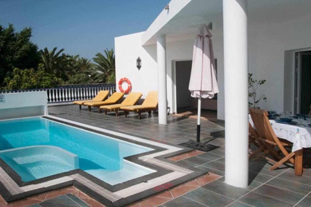 a pool with chairs and an umbrella next to a house at Villas del Mar Viña y Cabrera in Puerto Calero