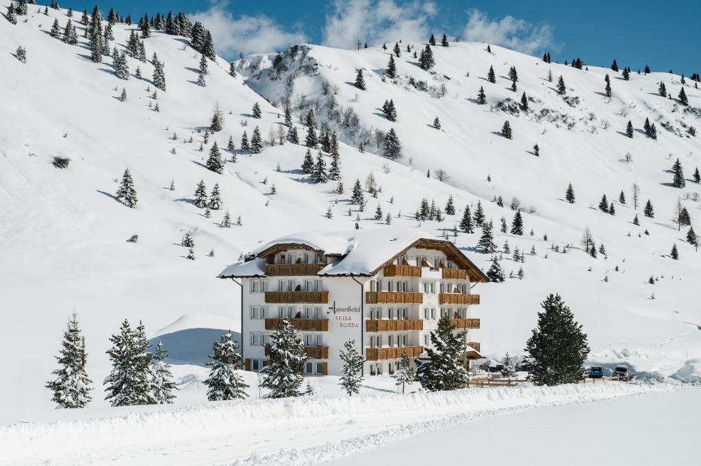 a building in the snow next to a mountain at Apparthotel Sellaronda in Arabba