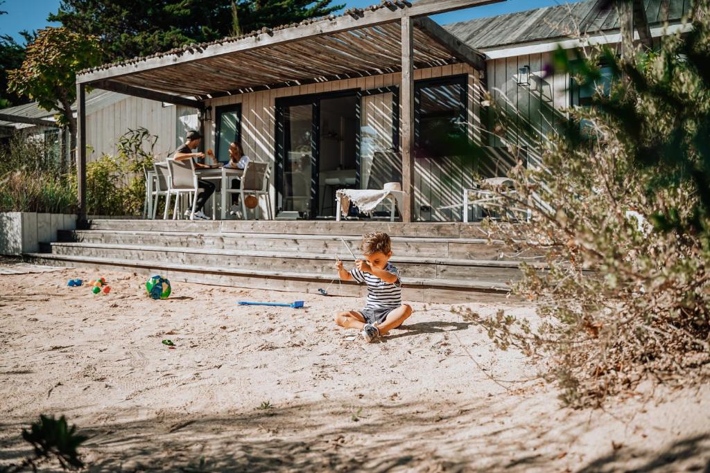 a young boy sitting in the sand in front of a house at Le Phare in Les Portes