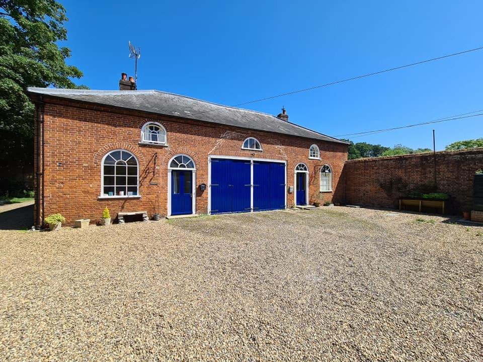 a brick building with blue doors on a gravel yard at Sloley Hall Cottages - Stable 1 in Tunstead