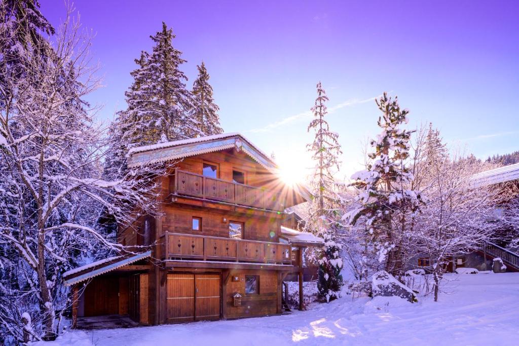 a log cabin in the snow with the sun shining at Chalet Côté Cœur, La Tania, with Outdoor Hot Tub and 7 Ensuite Rooms in La Tania