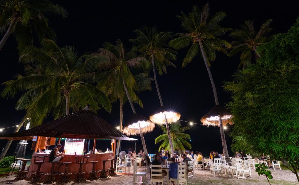 a group of people sitting at a bar on the beach at night at Beck's Resort in Haad Pleayleam