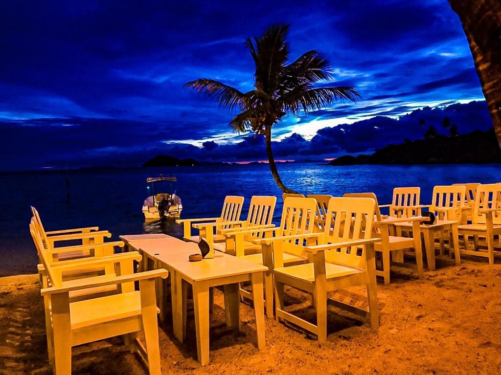 a group of tables and chairs on a beach with a palm tree at Beck's Resort in Haad Pleayleam