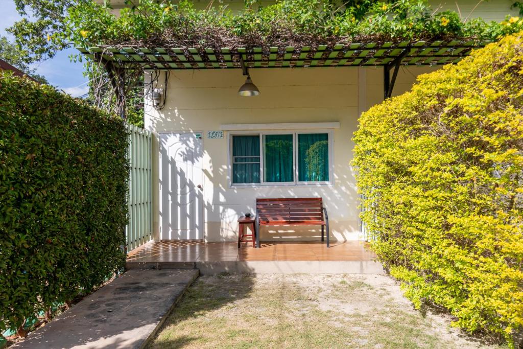 a white house with a bench in front of a hedge at บ้านสวนวารินทร์ รีสอร์ท in Pak Chong