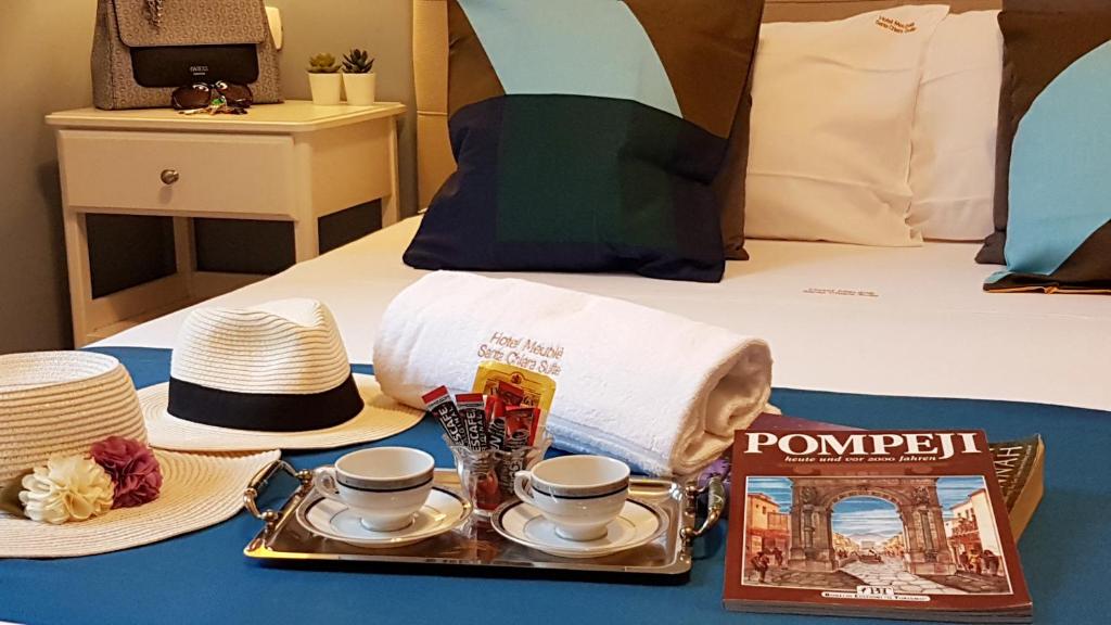 Una cama con una bandeja con sombreros y tazas y un libro en Hotel Meublè Santa Chiara Suite, en Nápoles