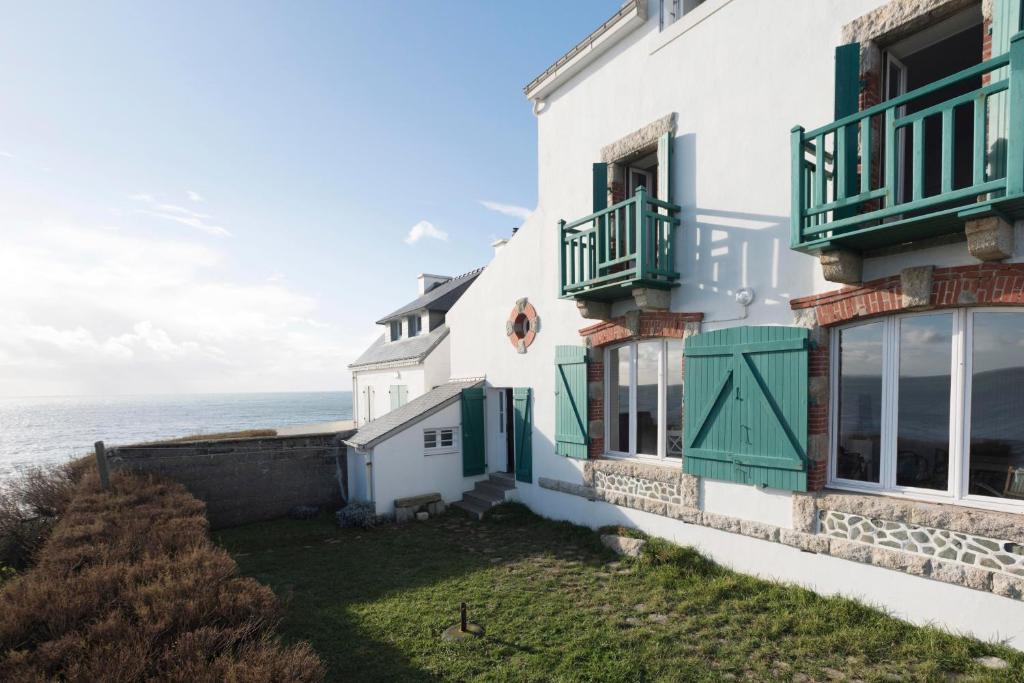 um edifício com persianas verdes e o oceano ao fundo em Villa des Roches - vue mer exceptionnelle em Clohars-Carnoët