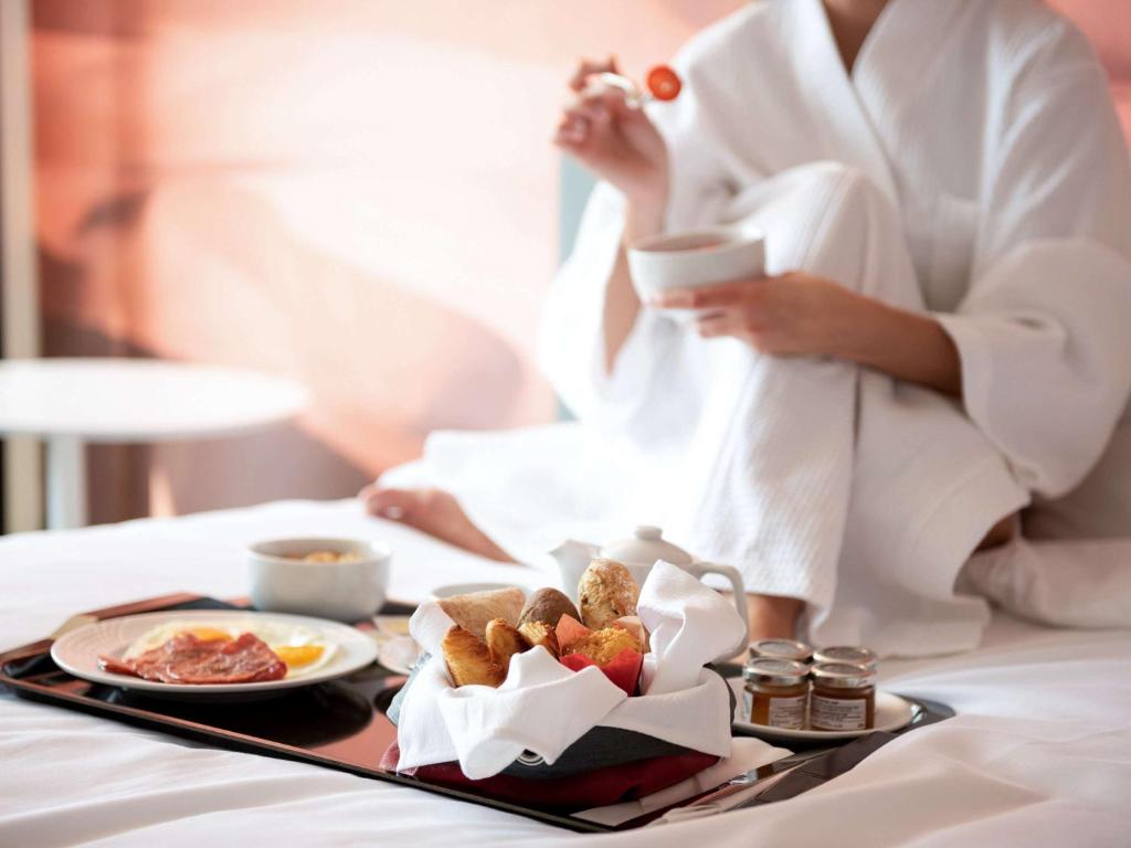 a woman in a hotel room with a tray of food at Novotel Sharjah Expo Centre in Sharjah