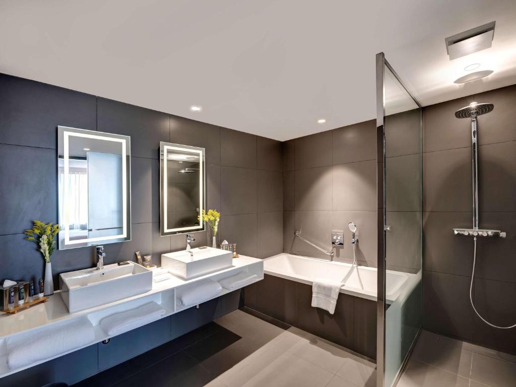 a bathroom with two sinks and two mirrors at Novotel Sharjah Expo Centre in Sharjah