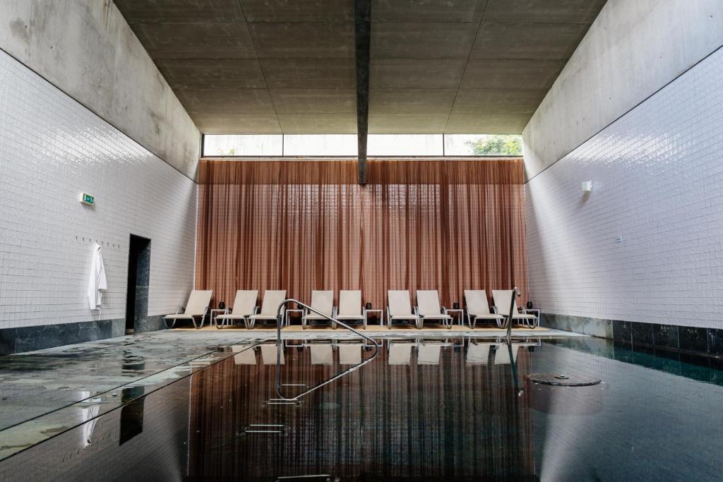 um quarto com uma piscina com cadeiras brancas e água em Axis Viana Business & SPA Hotel em Viana do Castelo