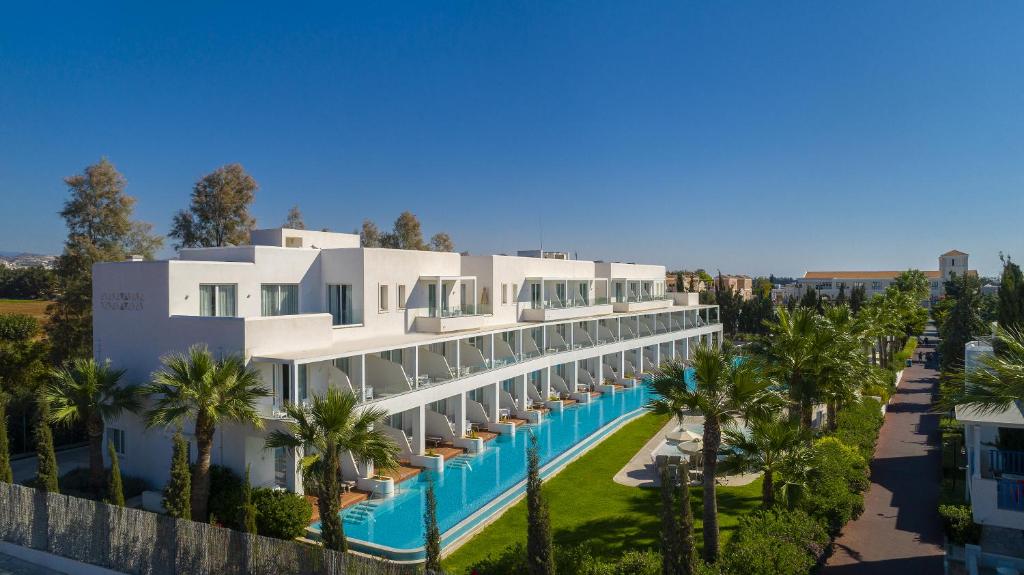 a large white building with a swimming pool and palm trees at Aliathon Aegean in Paphos