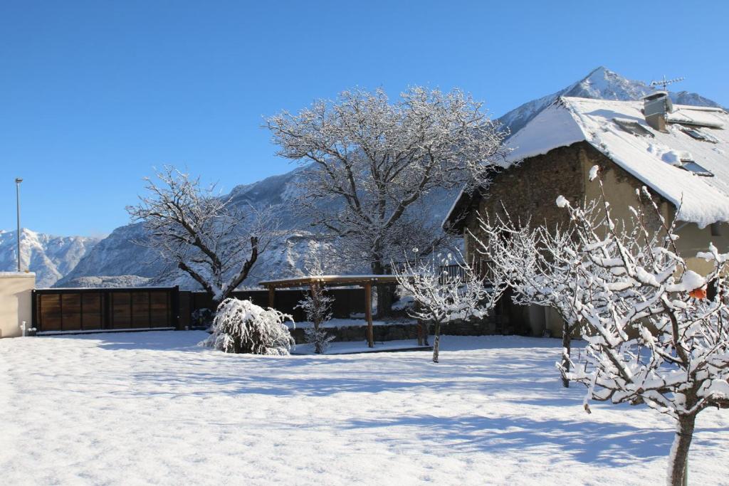 a house covered in snow with mountains in the background at Chambres d'hôtes Les Peschiers in Chateauroux-les-Alpes