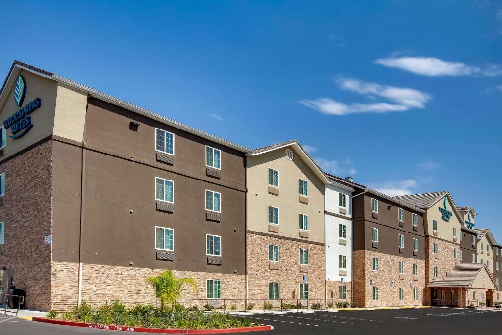 un grand bâtiment en briques avec un parking dans l'établissement WoodSpring Suites Bakersfield East, à Bakersfield
