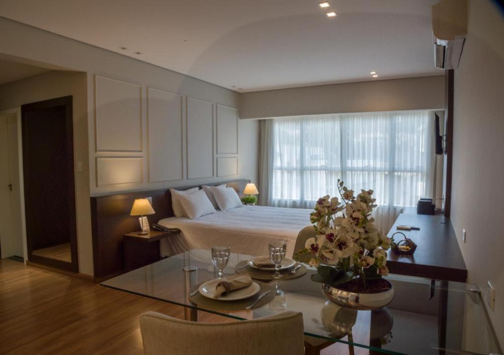 Santorini Hotel في Guanhães: غرفة نوم كبيرة مع سرير وطاولة مع طاولة زجاجية