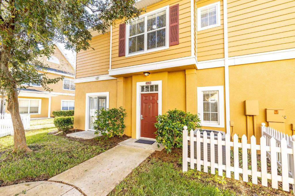 a yellow house with a white fence in front of it at Disney Townhouse with Themed Room in Kissimmee