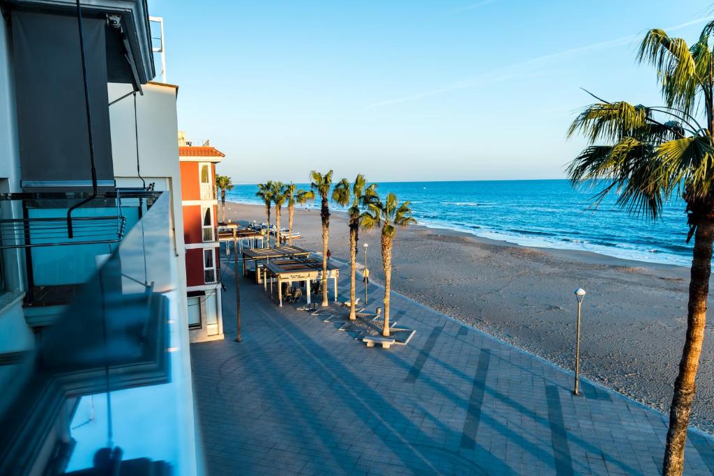 a view of a beach with palm trees and a building at Hauzify I Apartaments Grup Claustre in Torredembarra