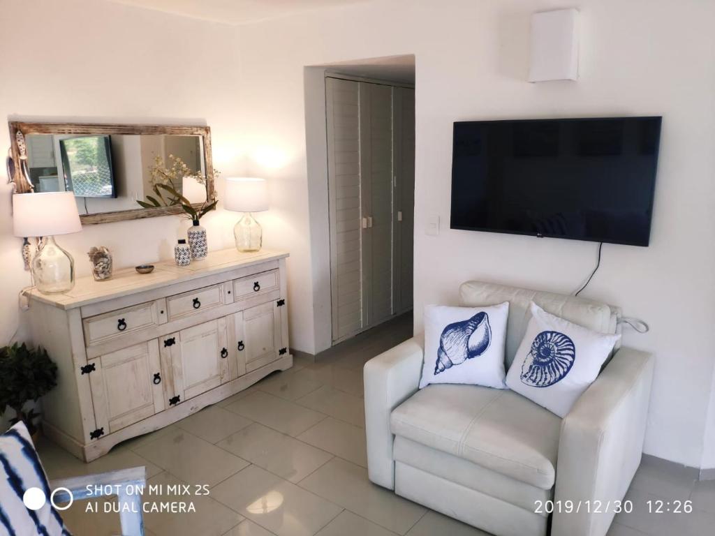 ein Wohnzimmer mit einem weißen Stuhl und einem Flachbild-TV in der Unterkunft Apartamento Marina de roosvelt con piscina climatizada in Punta del Este