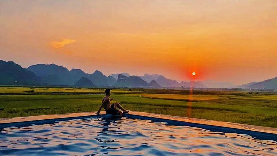 a man sitting in a pool with the sunset in the background at Karst Villas Phong Nha in Phong Nha