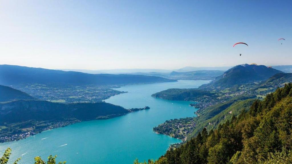 una vista di un lago con due parapendii che ci volano sopra di LA COSTIERE DU LAC - ANNECY - Vieille ville, Plage, Garage ad Annecy