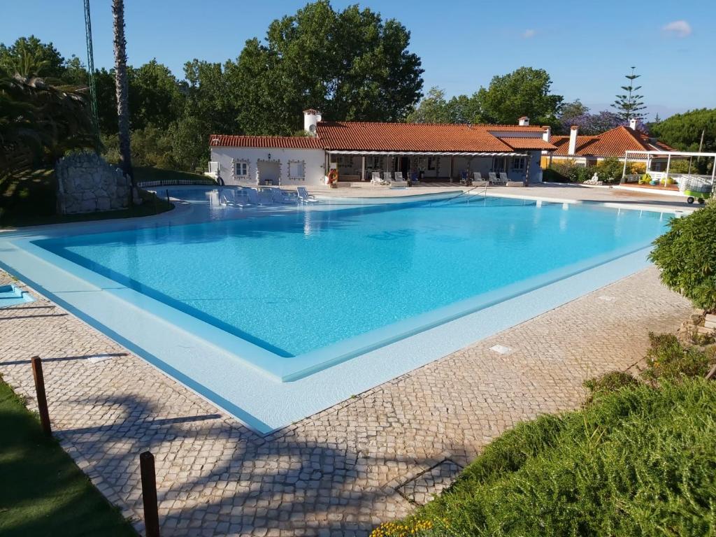 una gran piscina azul con una casa en el fondo en EPHYRUS - Country House, Restaurant, Wellness, en Setúbal
