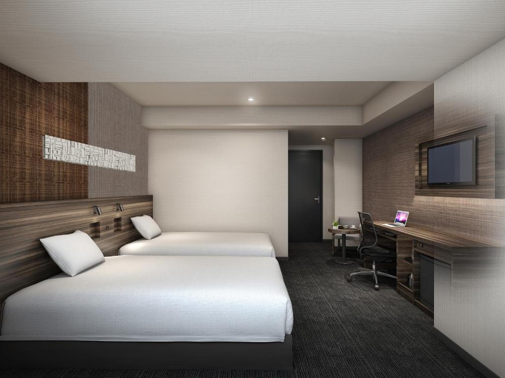 a hotel room with two beds and a desk at Smile Hotel Shin-osaka in Osaka